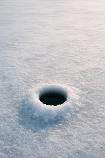 Single ice hole with a short rod resting next to it on the snow.