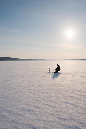 Wide snowy lake with anglers spread out under a pale winter sun.